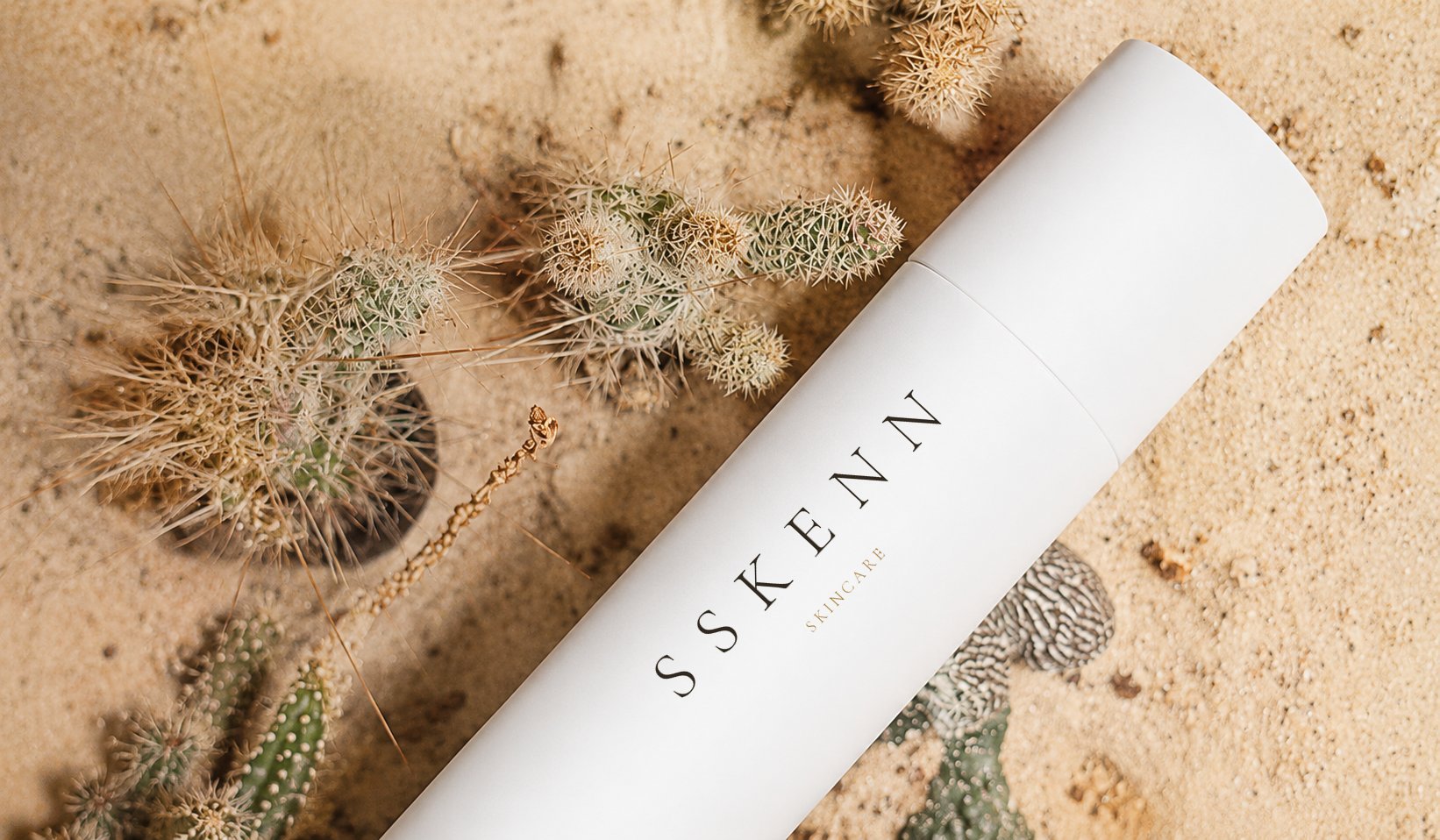 SSKENN skincare tube on warm sand among desert cacti